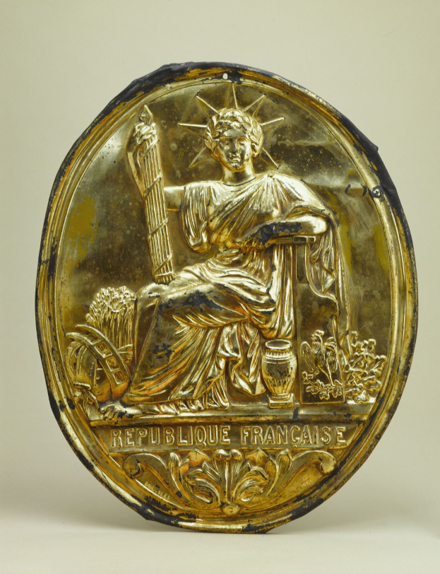 Goldene runde Plakette mit einem reliefartigen Abbild der Freiheitsstatue und eingraviertem Text auf einem weißen Hintergrund.