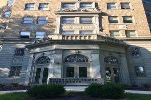 Großes Glasgebäude mit Textanzeige vorne, umgeben von grünem Gras und Pflanzen unter einem sichtbaren Himmel.