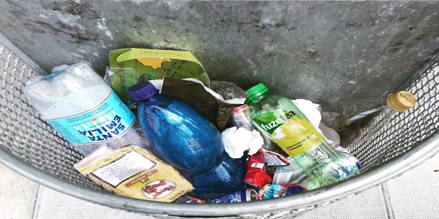 Ein Metallmüllcontainer voller Plastikflaschen, Tüten und anderer Gegenstände.