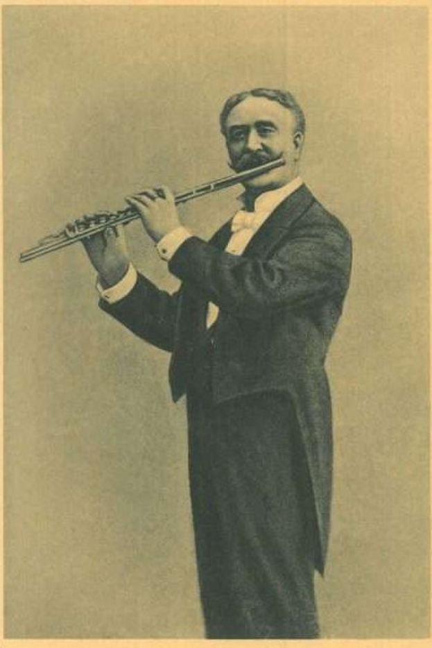 Ein Schwarz-Weiß-Foto eines Mannes in einem Smoking, der auf der Bühne eine Flöte spielt und dabei die Augen geschlossen hat und konzentriert ist, mit zurückgekämmtem Haar und von Scheinwerferlicht beleuchtet.