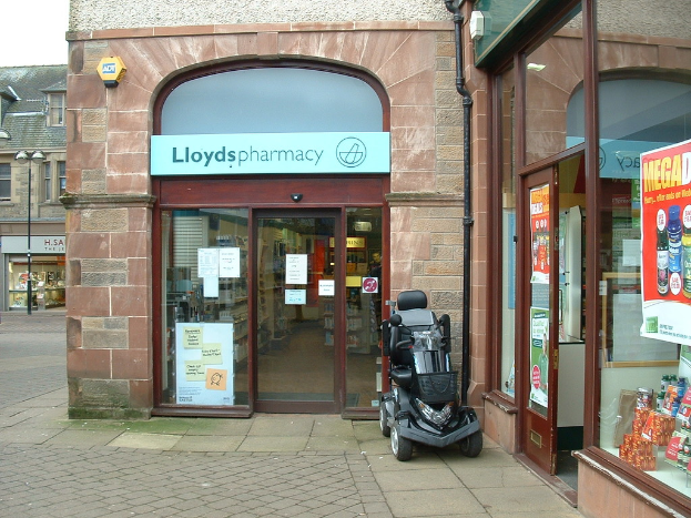 Eine Apotheke mit einem vor dem Gebäude geparkten Fahrzeug und einem Gebäude in der linken Ecke.