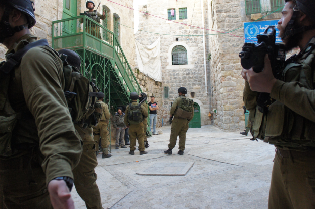 Israeli Soldaten in Helmen und Ausrüstung stehen in Jerusalems alter Stadt, einige halten Gewehre, mit Gebäuden und einem Banner im Hintergrund.