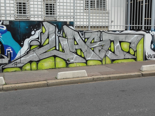 Eine Straße mit einem Gehweg und einer graffiti-bedeckten Wand neben einem Gebäude mit Fenstern und Gittern.