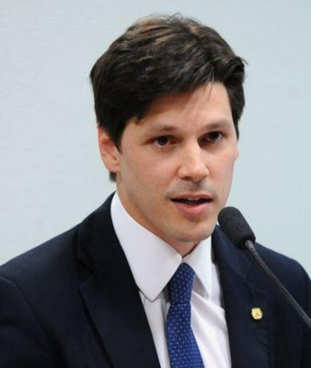 Ein Mann im Anzug und Krawatte spricht in ein Mikrofon vor einer Wand, wahrscheinlich um die Genehmigung eines Gesetzes durch die Regierung zu kommentieren.