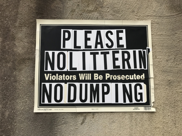 Schwarzes und weißes Schild an einem Gebäude mit der Aufschrift "Bitte keine Verschmutzung Verursacher werden verfolgt Keine Ablagerung".