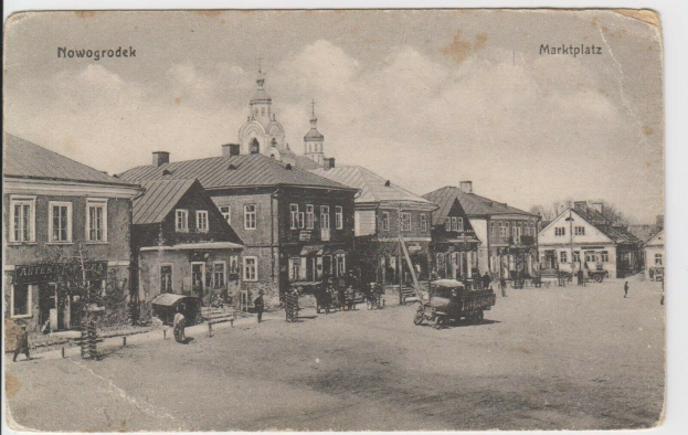 Schwarz-weiß-Foto einer Stadtstraße in Nowogrodeek, Deutschland, mit Gebäuden, Menschen, Karren, Pfählen, Bäumen und Himmel.