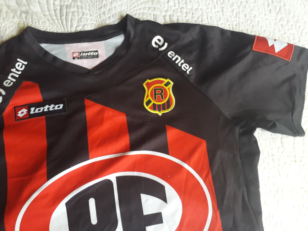 Schwarzer und roter Fußballjersey mit einer roten und schwarzen Streifen, mit einem Logo und Text auf einer weißen Oberfläche.