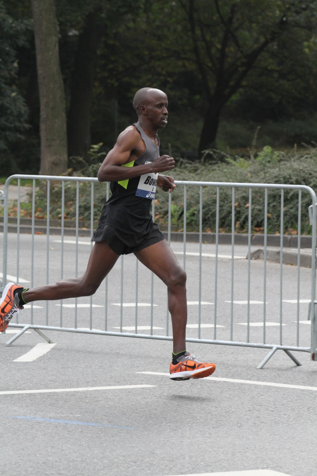 Ein Mann beim Marathonlaufen auf einer von B├Ąumen ges├Ąumten Stra├če, mit Sportschuhen bekleidet.