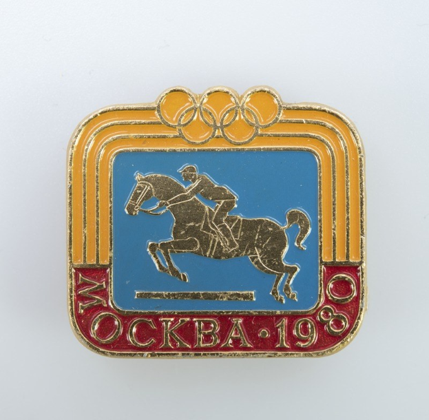 Olympisches Abzeichen von den Olympischen Winterspielen 1988 mit einer Person in weißem Hemd und blauen Shorts auf einem rotbraunen Pferd mit weißer Mähne und Schweif vor einem hellblauen Himmel mit weißen Wolken.