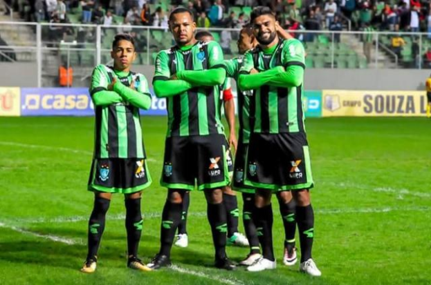 Männer in grün und schwarz feiern auf einem Füßballfeld, während Zuschauer aus der Stadiontribüne zuschauen.
