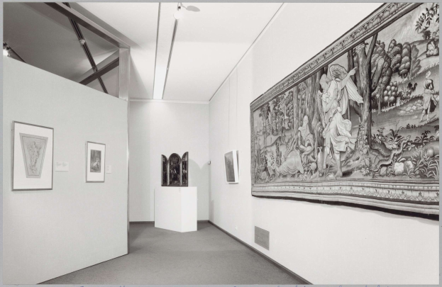 Schwarz-weißes Foto einer Museumsgalerie mit einem großen Wandteppich, gerahmten Kunstwerken, Sockeldisplays und Deckenleuchten, beschriftet mit "Museum of Fine Arts, New York City" unten.