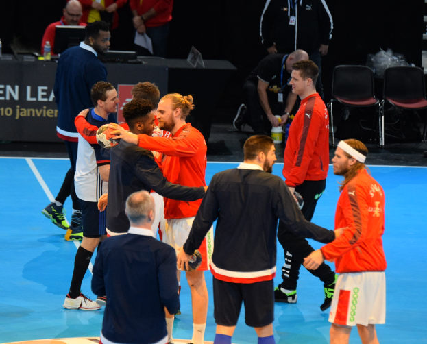 Mannengruppe auf einem Futsal-Platz mit Bällen, feiernd mit einem Tisch, Stühlen, Laptops, Flaschen und einer Tafel mit Text im Hintergrund.