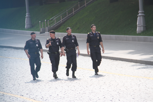 Drei Polizisten in Uniform, die eine Straße entlanggehen, mit Pfosten, Geländern, Treppen und Gras im Hintergrund.