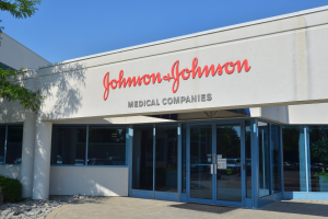 Das Johnson & Johnson Medical Companies-Gebäude mit Glaswänden und -türen, das Text an der Wand, Steine, Pflanzen und einen Baum auf der linken Seite zeigt, vor einem klaren blauen Himmel.