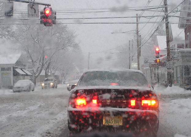 Eine ruhige, schneebedeckte Straße, gesäumt von Häusern und Bäumen mit wenigen Fahrzeugen.