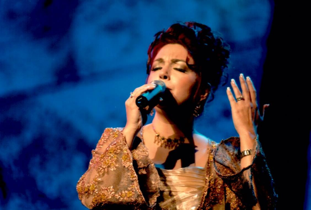 Eine Frau in einem goldenen Kleid, die auf der Bühne in ein Mikrofon singt, vor einem blauen und schwarzen Hintergrund, bei der Eurovision Song Contest.