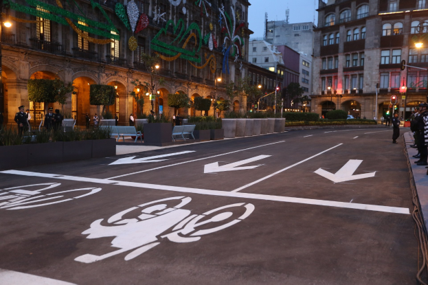Stadtstraße mit einem Fahrradweg, umgeben von Gebäuden, Straßenmöblierung, Fußgängern, Grünflächen und einem klaren blauen Himmel.