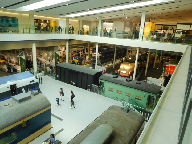 Ein großer Museumsraum mit verschiedenen Arten von Zügen, Menschen, Geländern, Säulen, Lampen und Informationsschildern.