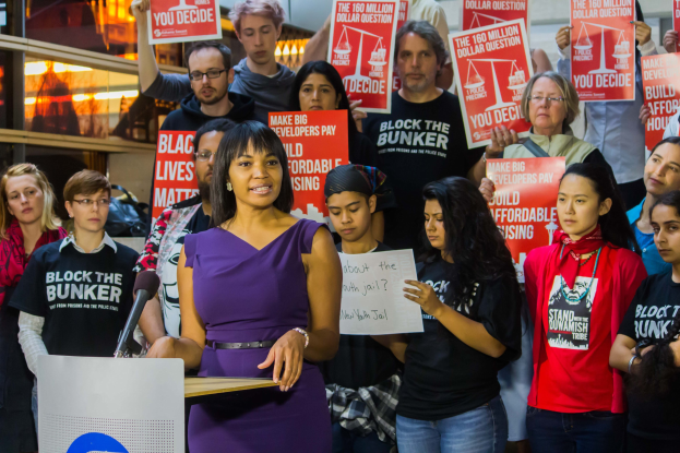 Eine Black-Lives-Matter-Aktivistin spricht an einem Rednerpult mit Mikrofon vor einer Menge mit Schildern.