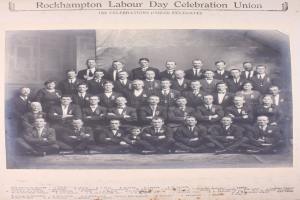 Gruppe von Menschen in Blazern und Krawatten, die für ein Foto posieren mit "Rockhampton Labour Day Celebration Union" Text oben und unten.