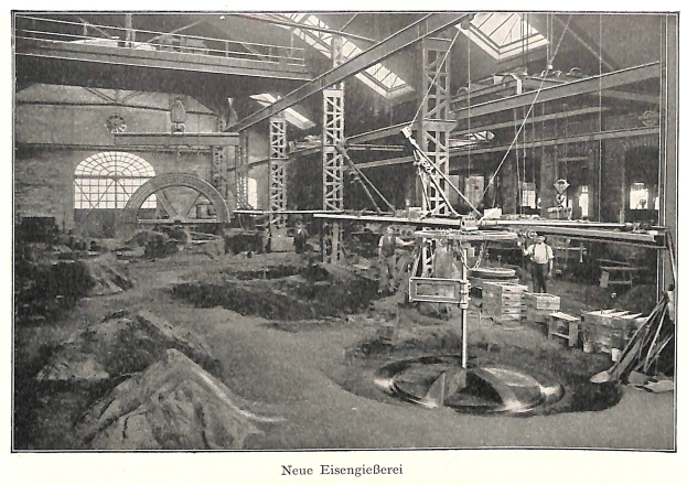 Schwarzes und weißes Foto einer Fabrikhalle mit Arbeitern, die an einer Maschine arbeiten, umgeben von Metallstangen und -rohren, beschriftet mit 'Neue Eisenglebeerei, die erste Fabrik in Deutschland' unten.