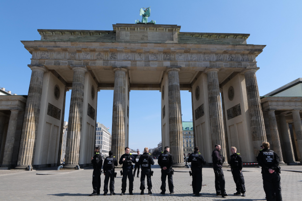 Eine Gruppe von Polizisten vor dem Brandenburger Tor in Berlin, Deutschland, mit sichtbarem Torbogen, Säulen und Statue, umgeben von Gebäuden und einem sichtbaren Himmel.