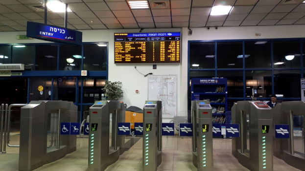 Ein Mann steht vor einer Metalldrehsperre am Flughafen, mit Metalldetektoren, Hinweistafeln, einem Topf mit Pflanze, einer Wandtafel, Deckenleuchten und einem Anzeigebildschirm im Hintergrund.