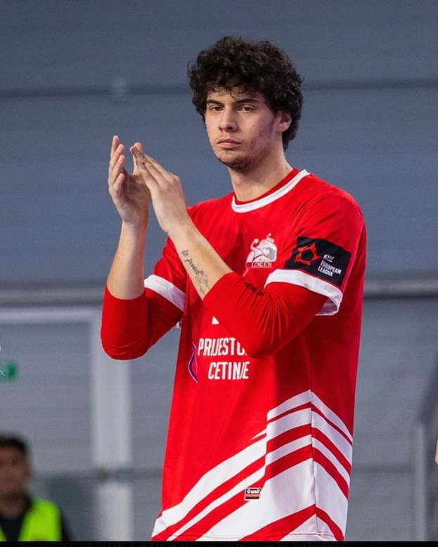 Ein Mann in einem roten und weißen Hemd klatscht in den Händen im Vordergrund mit einer anderen Person und einer Wand im Hintergrund; Text unten lautet 'Kopenhagen Futsal Club - Foto 1'.