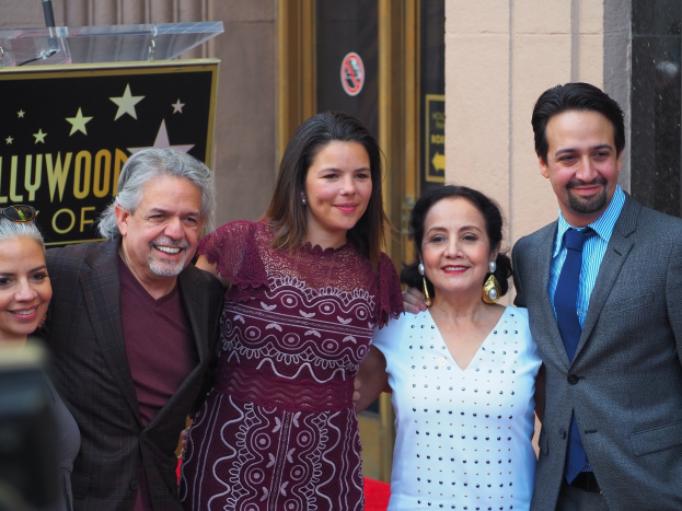 Gruppe von Menschen, die auf einem roten Teppich bei der Zeremonie des Hollywood Walk of Fame posen, mit einer Tafel, einem Glaspodium und einer Wand im Hintergrund.