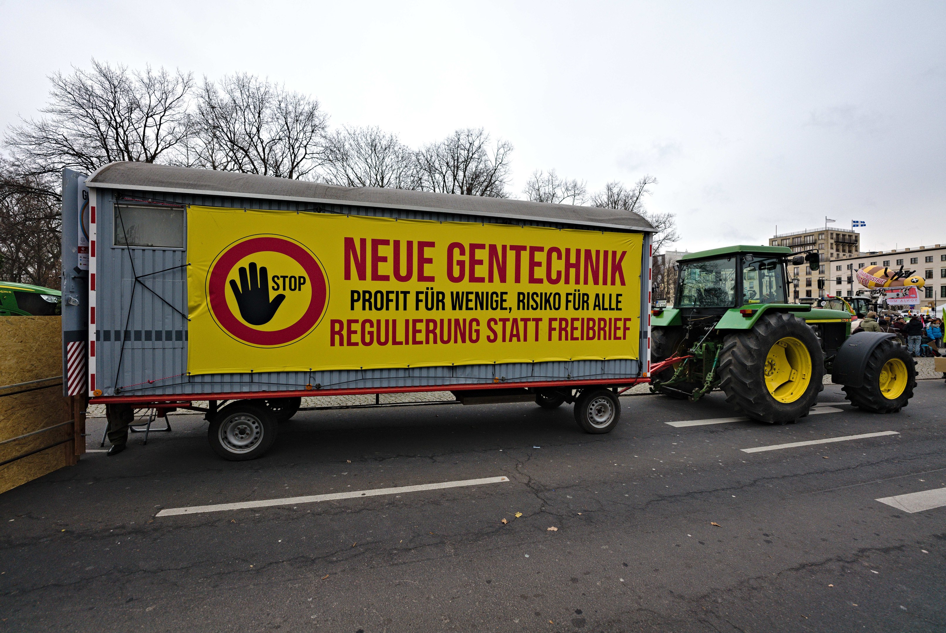 A truck with a sign driving down a street during a demonstration in Germany, surrounded by people, trees, buildings, and a clear blue sky.