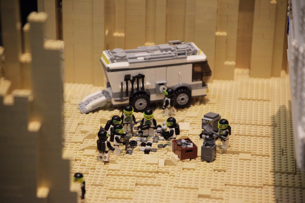 Lego-Modell einer Star-Wars-Szene mit einem Landfahrzeug im Vordergrund und verstreuten Spielzeugen sowie einer Wand im Hintergrund.