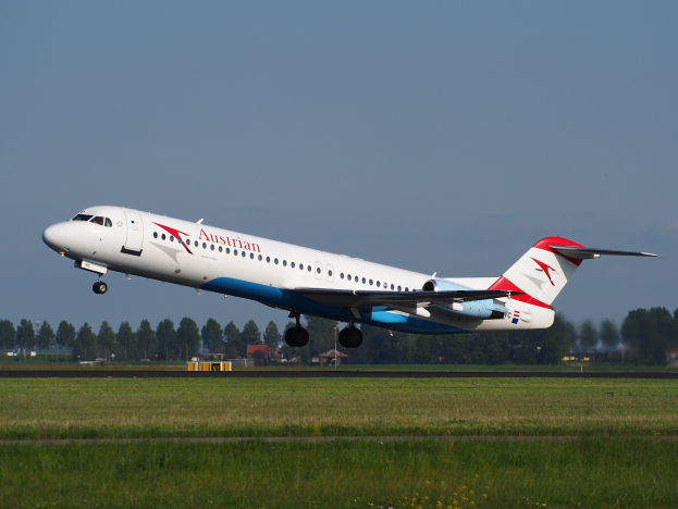 Austrian Airlines Embraer ERJ-190 Flugzeug startet am Frankfurter Flughafen, mit grünem Gras, Bäumen, Gebäuden und Himmel im Hintergrund.