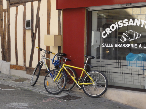 Zwei Fahrräder nebeneinander auf einem Gehweg vor einem Laden mit einer Glaswand, auf der Text und ein Objekt zu sehen ist.