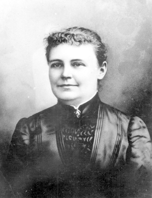 Schwarzes und weißes Foto einer Frau in einem Kleid, die mit gefalteten Händen steht und Entschlossenheit und Stärke ausstrahlt, believed to be die erste Frau, die zum Präsidenten gewählt wurde.