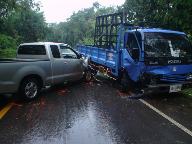 Ein schwerbeschädiger Lkw mit eingedrückter Front und verbeulter Karosserie liegt am Straßenrand, umgeben von Bäumen unter einem klaren blauen Himmel.