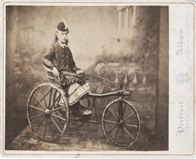 Schwarzes und weißes Foto einer Frau auf einem Fahrrad mit einem Kleid und einer Mütze, mit Text auf der rechten Seite.