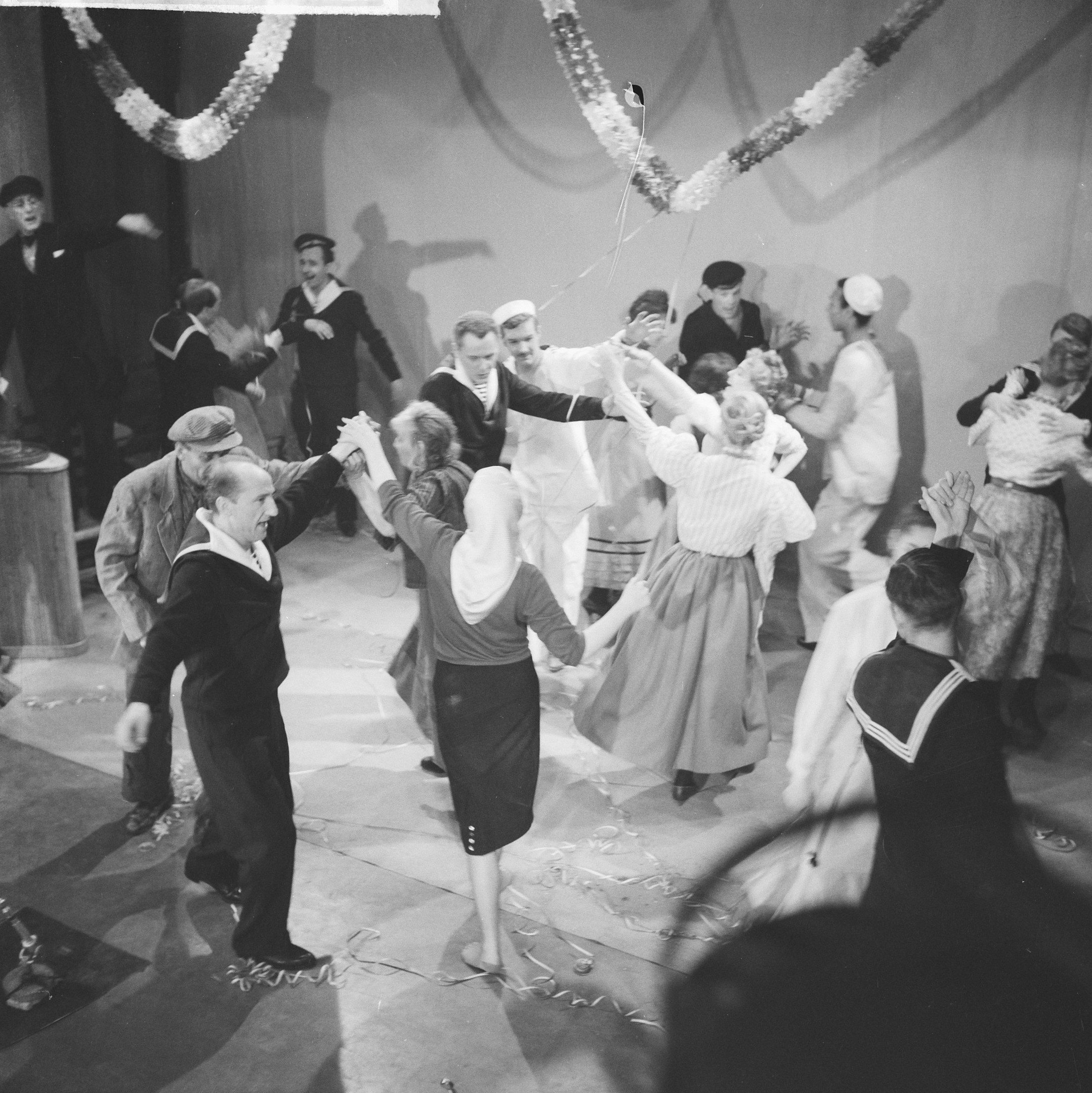Schwarz-weißes Bild von Menschen, die auf einer Tanzfläche tanzen, mit einem Tisch und einer dekorativen Wand im Hintergrund.
