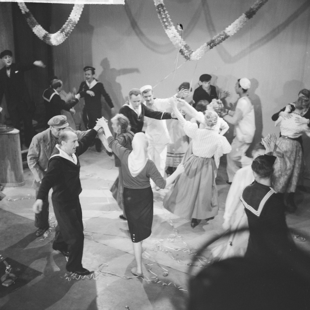 Schwarz-weißes Bild von Menschen, die auf einer Tanzfläche tanzen, mit einem Tisch und einer dekorativen Wand im Hintergrund.