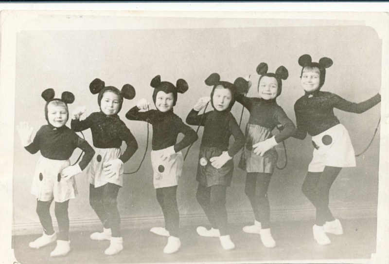Eine Gruppe von Kindern in schwarzen und weißen Mickey-Maus-Kostümen, die zusammen in einem Fotorahmen posieren, tragen passende Mickey-Maus-Ohren und Schuhe.