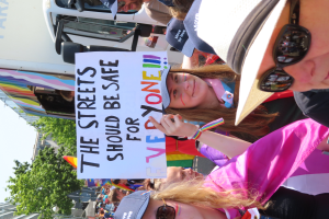 Eine Gruppe von Menschen steht vor einem Lastwagen und hält ein Schild hoch, auf dem "Die Straßen sollten sicher sein" steht. Einige tragen Mützen und Schutzbrillen, andere halten Schilder, vor einem Hintergrund aus Bäumen, Gebäuden und einem klaren blauen Himmel.