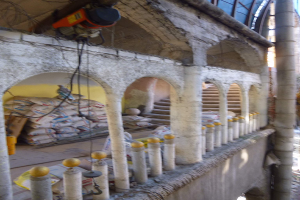 Ein altes Gebäude mit Bögen und Säulen wird renoviert, mit Werkzeugen, Materialien und verstreuten Gegenständen drumherum, darunter Taschen, Geländer und eine Maschine mit Drähten oben.