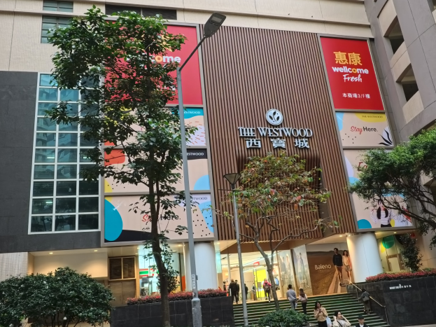 Außenansicht des Westwood Shopping Centre in Hong Kong, mit Gebäuden, Straßeninfrastruktur, Grünflächen, Fußgängern, Treppen und Beschilderung.