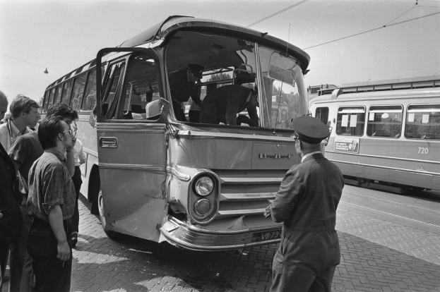 Schwarzes und weißes Bild eines verunglückten Busses auf der Straße mit einer Gruppe von Menschen drumherum und anderen Fahrzeugen im Hintergrund.