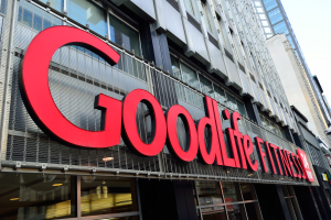 Ein Goodlife Fitness-Studio in New York City mit Glaswänden und einer Namensplakette, umgeben von anderen Gebäuden unter einem sichtbaren Himmel.