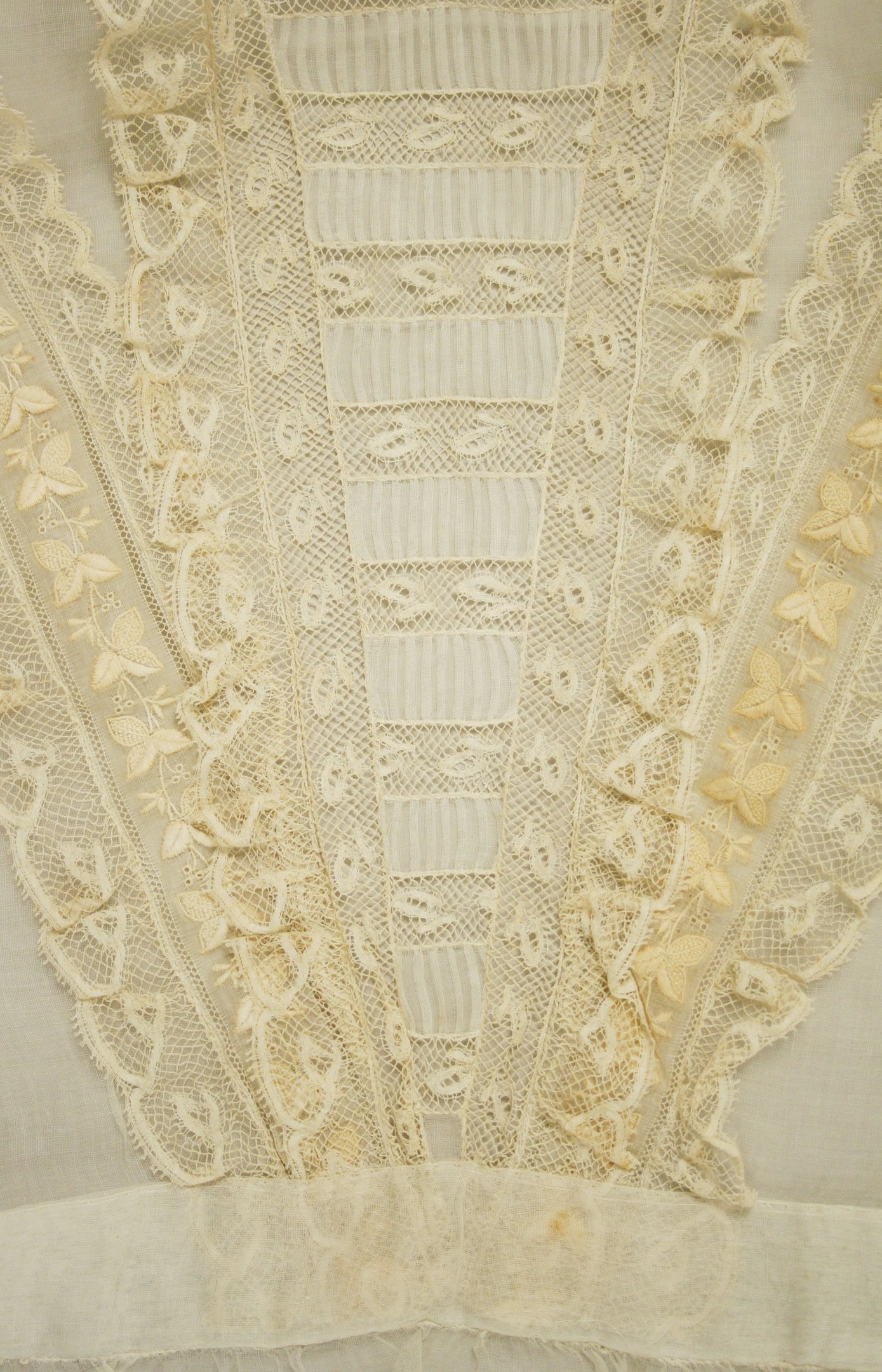 Nahaufnahme eines weißen Kleides mit zarter, detailreicher Spitzenverzierung in verschiedenen Formen und Mustern, aus leichtem, luftigem Sommergewebe.