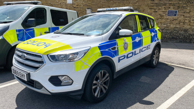 Zwei Polizeiwagen nebeneinander auf einem Parkplatz geparkt, mit einer Wand und einem Schild im Hintergrund.