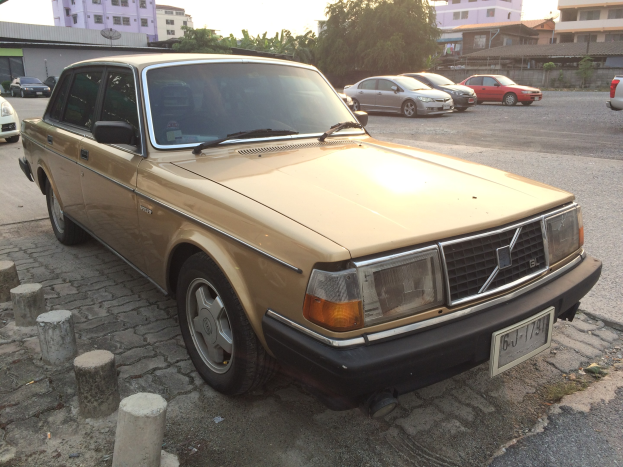 Ein goldfarbener Wagen, der auf der Straße neben Gebäuden, Bäumen und einem klaren blauen Himmel geparkt ist.