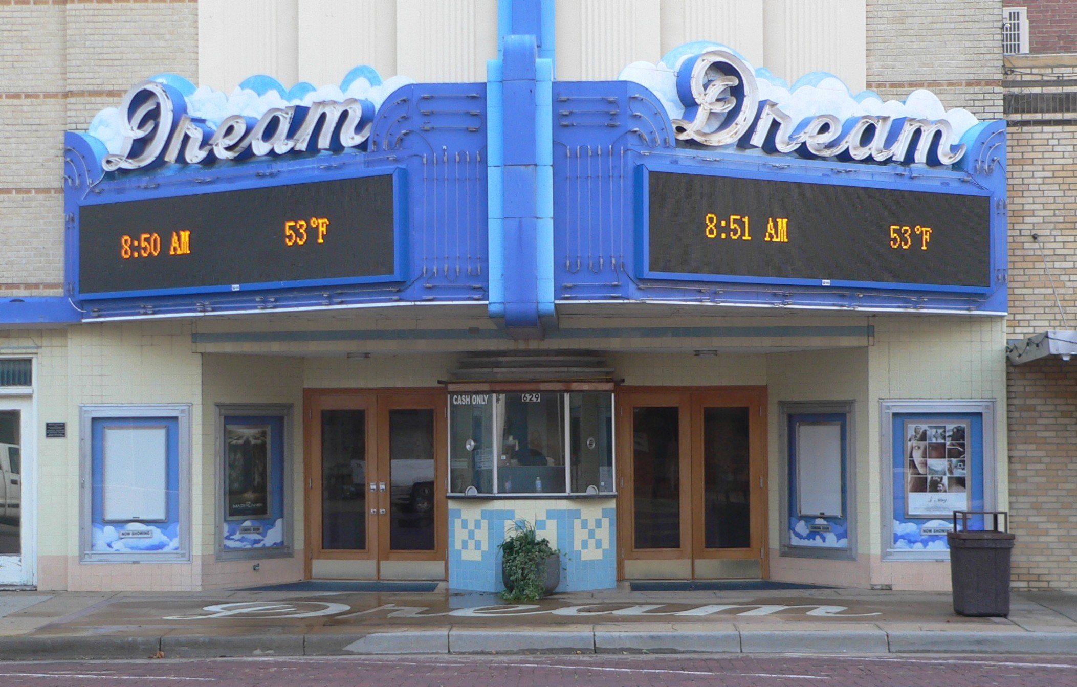 Außenansicht des Dream Theaters in St. Louis, Missouri, mit Glastüren und -fenstern, einem Namen Schild, einem Müllbehälter, einem Topf mit einer Pflanze und einer Straße unten.