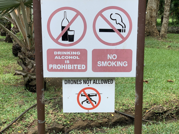 Schilder am Straßenrand mit der Aufschrift "Alkoholtrinken verboten" und "Rauchen verboten" mit Bäumen und Gras im Hintergrund.