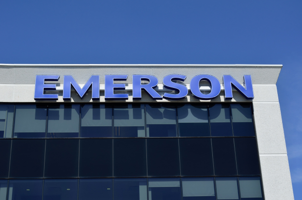 Das Emerson-Logo an der Seite eines Gebäudes mit dem Text "Emerson investiert 1,5 Milliarden US-Dollar in den USA" vor einem klaren blauen Himmel.
